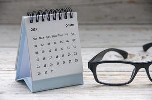 calendrier de bureau blanc d'octobre 2023 sur une table en bois avec fond de lunettes. photo