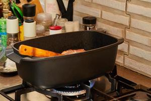 morceau de viande est frit avec des oignons dans une sauce au vin dans une casserole rectangulaire au feu sur une cuisinière à gaz. photo