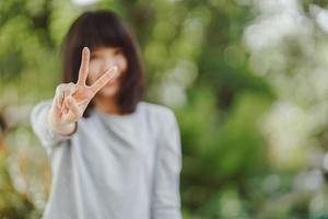 femme heureuse sourire avec v signe geste de la main avec fond de nature, concept de signe de victoire et de paix. mise au point sélective. photo