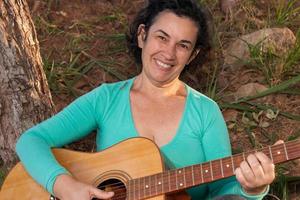 heureux femmes matures jouant et chantant sa guitare acoustique dans le parc photo