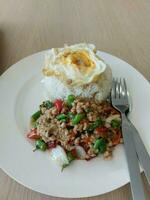 du riz et du basilic sauté avec du porc haché et des œufs frits étaient servis sur une assiette blanche. photo