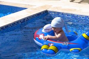 .un enfant flotte dans un cercle de caoutchouc gonflable en forme d'avion. un enfant dans une piscine extérieure à l'eau bleue, photo