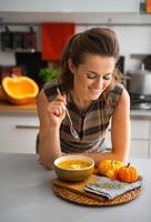 jeune femme au foyer, manger de la soupe de potiron dans la cuisine photo