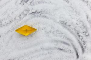 Bateau en papier jaune sur une surface inégale de neige photo