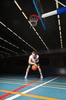 jeune homme sain et dur jouant au basket-ball dans la salle de gym intérieure. photo