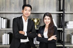 souriant jeune homme d'affaires et femme d'affaires portent un costume bras croisés sur fond de bureau moderne, entreprise prospère photo