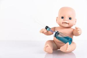 la poupée bébé tient une seringue médicale et une ampoule avec un vaccin. concept de vaccin pour les nouveau-nés. espace de copie. photo