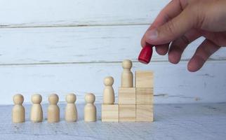 personnages en bois sur des blocs de bois avec une main tenant une poupée à figures rouges. notion d'entreprise photo