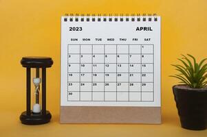 calendrier de bureau d'avril 2023 avec plante de table et verre de minutes sur fond jaune. photo