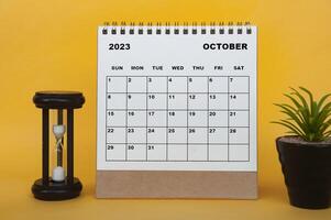 calendrier de bureau d'octobre 2023 avec verre de minutes et plante sur fond jaune. photo