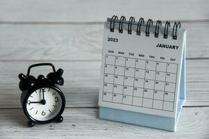 janvier 2023 calendrier de bureau blanc avec réveil noir pointant à 9 heures sur table en bois.