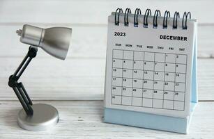 décembre 2023 calendrier de bureau blanc avec lampe de table sur table en bois. photo