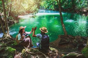 voyageurs, couples avec sacs à dos, assis et se détendre sur les rochers. voyagez dans la nature dans la jungle verte et profitez de la vue sur la cascade. tourisme, randonnée, étude de la nature. couples voyageant, prenant des photos