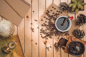 café noir et grains de café avec boussole, carte du monde sur le fond en bois de la table. concept de voyage photo