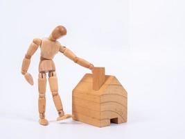 l'homme s'appuya contre le modèle d'une maison isolée sur fond blanc. concept avec une marionnette en bois photo