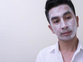 beau jeune homme asiatique appliquant de la crème sur son visage avec un visage souriant, concept de soins de la peau photo