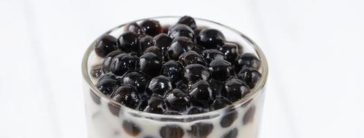 thé au lait à bulles avec garniture de perles de tapioca, célèbre boisson taïwanaise sur fond de table en bois blanc dans un verre à boire, gros plan, espace de copie photo