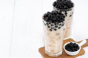 thé au lait à bulles avec garniture de perles de tapioca, célèbre boisson taïwanaise sur fond de table en bois blanc dans un verre à boire, gros plan, espace de copie photo