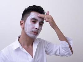 beau jeune homme asiatique appliquant de la crème sur son visage avec un visage souriant, concept de soins de la peau photo