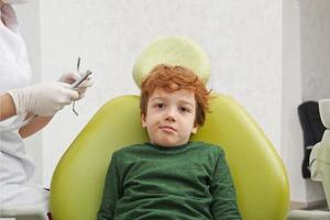 petit garçon mignon assis sur une chaise chez le dentiste photo