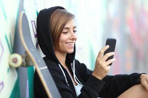 jeune patineuse heureuse adolescente à l'aide d'un téléphone intelligent photo