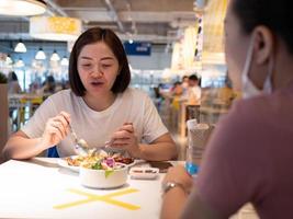 femme asiatique assise séparée dans un restaurant mangeant de la nourriture avec une cloison en plastique de protection de table pour protéger l'infection par le coronavirus covid-19 photo