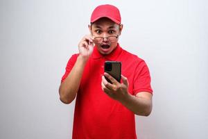 un livreur asiatique portant une chemise rouge semble surpris de la bonne nouvelle qu'il a reçue de son smartphone.
