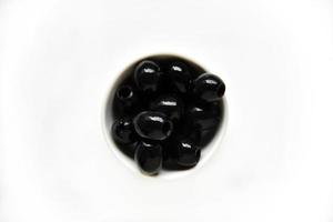 olives noires dans une casserole blanche et en verre sur fond blanc. photo