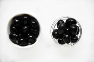 olives noires dans une casserole blanche et en verre sur fond blanc. photo