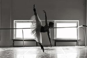 une charmante ballerine en body pose des éléments de ballet dans une coiffe dans un studio photo