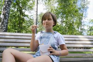 une adolescente en promenade un jour d'été dans le parc déjeune avec des nouilles au wok photo