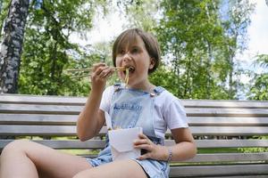 une adolescente en promenade un jour d'été dans le parc déjeune avec des nouilles au wok photo