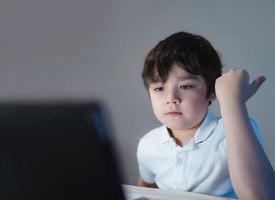 un écolier heureux s'amusant à regarder des dessins animés sur une tablette, un enfant utilisant un pavé numérique recherchant les idées sur Internet pour ses devoirs, l'enseignement à domicile, l'apprentissage à domicile ou l'apprentissage en ligne photo