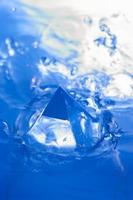 fond bleu abstrait avec des éclaboussures d'eau et un objet géométrique. pyramide dans l'eau. photo