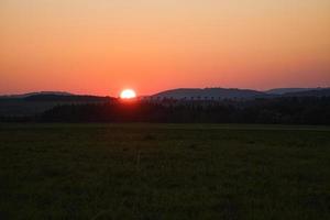 coucher de soleil romantique derrière une colline devant un pré. photo