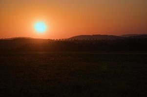coucher de soleil romantique derrière une colline devant un pré. photo