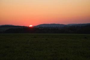 coucher de soleil romantique derrière une colline devant un pré. photo