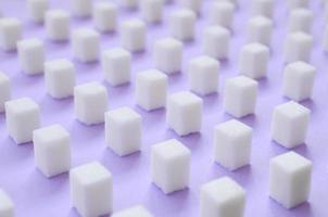 de nombreux petits cubes de sucre sont alignés sur un fond violet. photo