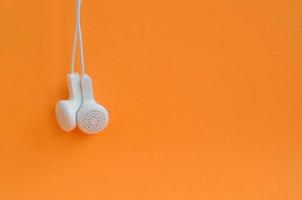 écouteurs modernes blancs suspendus sur un fond orange vif photo