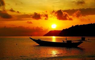 silhouette d'un bateau à longue queue se garant sur la mer avec un ciel orange, des nuages de montagne et un fond de lever de soleil tôt le matin photo