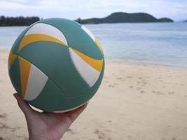 une main tenant le volley-ball de plage avec fond de plage photo