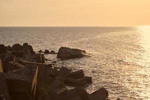 paysage marin avec de grands brise-lames en béton au beau coucher de soleil orange, vagues de la mer au soleil du soir photo