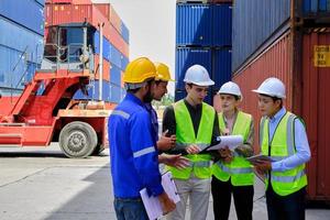 un groupe de travailleurs multiraciaux portant des uniformes de sécurité et des casques durs travaillent au terminal logistique avec de nombreuses piles de conteneurs, chargeant des marchandises d'expédition de contrôle pour l'industrie du transport de fret. photo