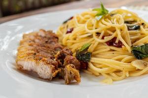 Des spaghettis sautés à la thaïlandaise avec sauce au piment séché et des escalopes de porc chaudes, tendres et délicieuses sont servis dans une assiette blanche sur une table en bois, ce qui donne des spaghettis épicés et des escalopes de porc parfumées. photo