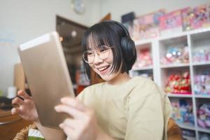 jeune femme asiatique adulte portant un casque écouter de la musique et se détendre à l'aide d'une tablette numérique pour surfer sur le net photo