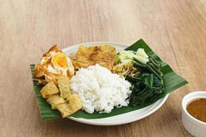 nasi pecel, un riz javanais traditionnel avec salade de légumes et sauce aux cacahuètes, servi avec des plats d'accompagnement tels que des œufs, du martabak et des craquelins peyek. photo