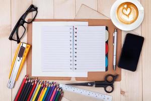 un cahier vierge ouvert avec des crayons de couleur, un stylo, un smartphone et une tasse de café sur une table en bois photo