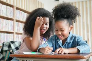 Dessin d'enfant d'âge préscolaire avec un crayon de couleur sur du papier blanc sur une table en classe avec des amis photo