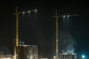 grues à tour et immeubles à plusieurs étages inachevés près des bâtiments en construction dans la nuit photo