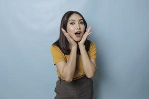 une femme asiatique surprise s'allonge sur ses mains et crie tout en regardant la caméra sur fond bleu photo